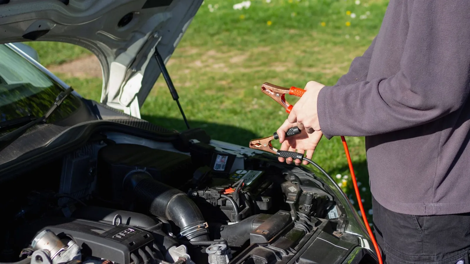Neue Autobatterie wird im Motorraum eingesetzt, Polklemmen liegen bereit